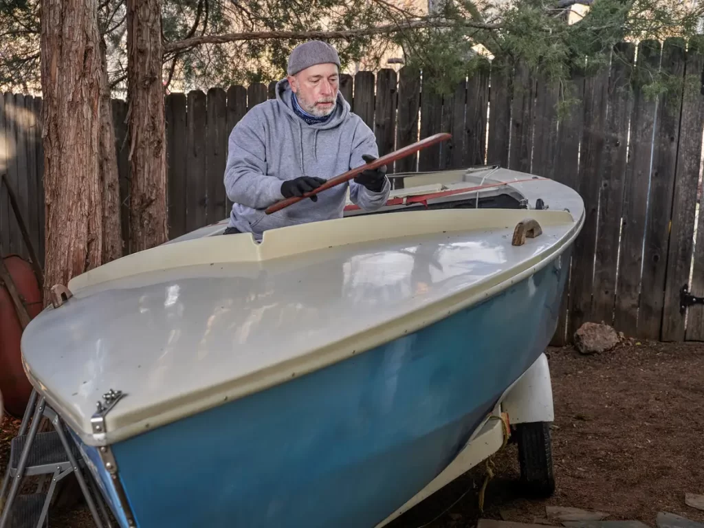 Senior male sailor is working on his sailing dinghy parked on a trailer in backyard.