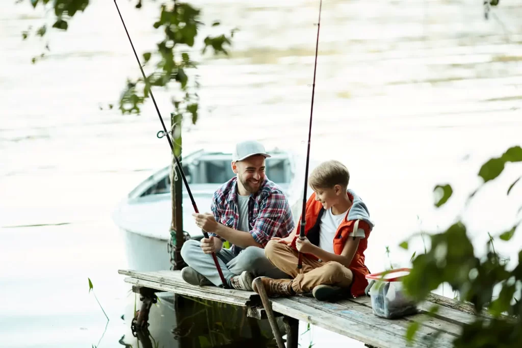 Happy father sitting with his son on the pier and fishing during summer vacation