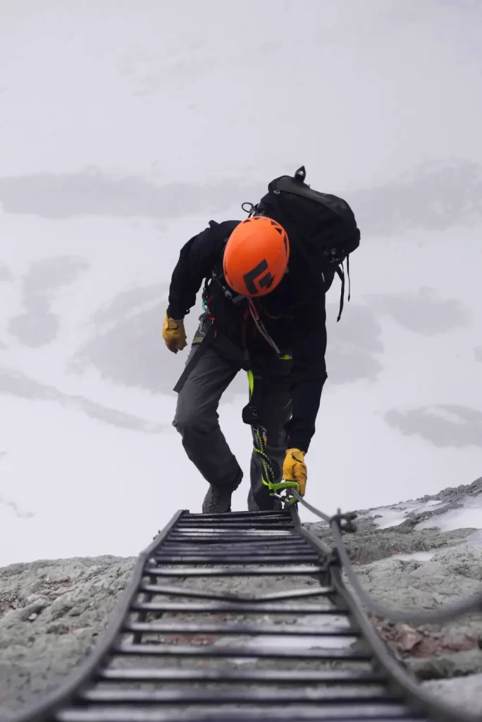 A hiker moving up on a ladder on a mountain during winter.